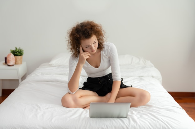 Die junge Frau, die mit ihrem Laptop auf dem Bett im Schlafzimmer sitzt, hat ein Problem