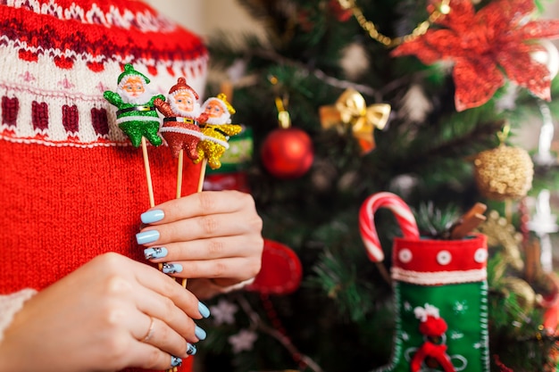 Die junge Frau, die Spielwaren Sankt hält, formte durch den Weihnachtsbaum zu Hause und trug Winterstrickjacke.