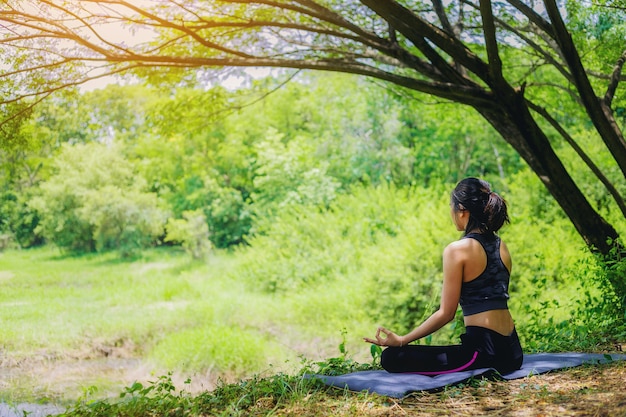 Die junge Frau, die Yogahaltung unter dem Baum tut, schließen die Natur