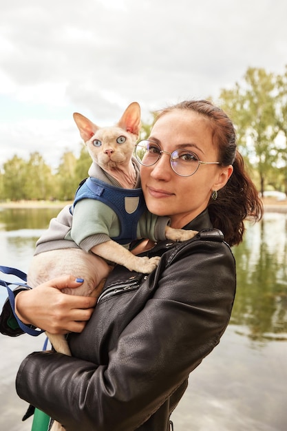 Die junge Frau hält ihre Katze in Amoveralls auf ihren Füßen Katze auf einem Spaziergang Liebe zu den Tieren Closeup