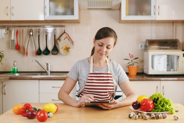 Die junge Frau schneidet in der Küche mit Messer und Laptop auf dem Tisch Gemüse. Gemüsesalat. Diät-Konzept. Gesunder Lebensstil. Kochen zu Hause. Essen zubereiten.