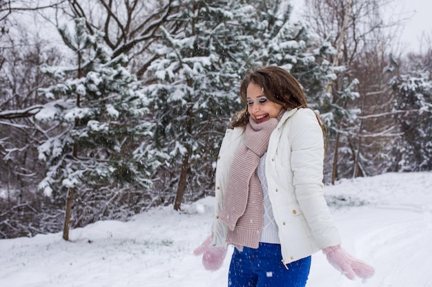 Die junge Frau wirft Schnee und lächelt Frau in warmer Kleidung freut sich im Winter im Freien