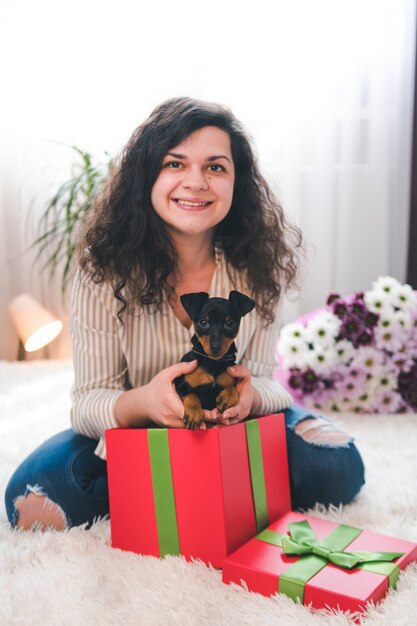 Die junge glückliche Frau nimmt den süßen kleinen Welpen der Geschenkbox heraus. Schwarzbrauner Zwergpinscher in der Hand des Weibchens