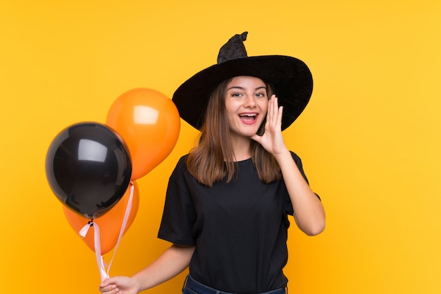 Die junge Hexe, die schwarze und orange Luftballone für Halloween-Parteien schreit mit dem breiten Mund hält, öffnen sich