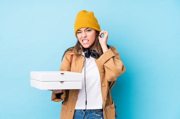 Die junge kaukasische Frau, die Pizzas hält, lokalisierte Bedeckungsohren mit den Händen.