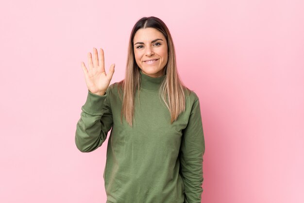 Die junge kaukasische Frau lokalisierte das Lächeln nett, Nr. Fünf mit den Fingern zeigend.