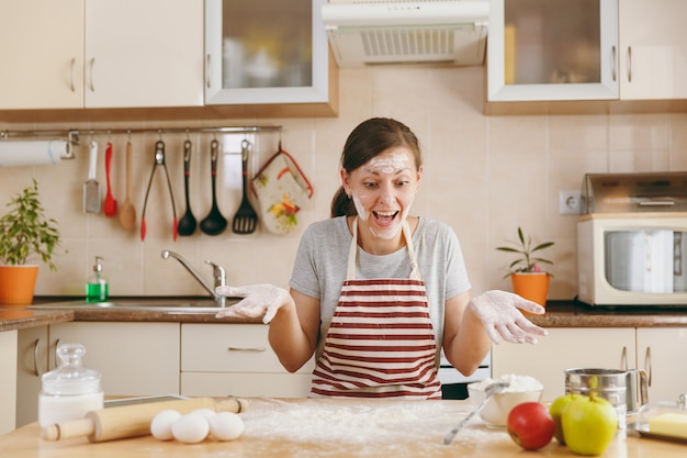 Die junge lustige fröhliche Frau sitzt an einem Tisch mit Mehl und bereitet einen Kuchen in der Küche zu. Kochen nach Hause. Essen zubereiten.