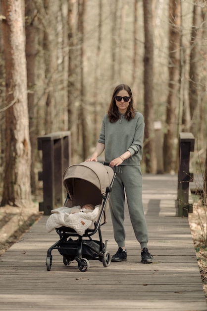 Die junge Mutter geht mit ihrem Kleinkind, das im Kinderwagen schläft, auf dem Holzsteg Die Mutter mit ihrem Kind im Park an der frischen Luft