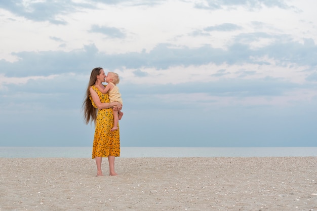 Die junge Mutter umarmt sanft ihre Tochter und küsst sie. Mutter und Baby auf See Hintergrund.