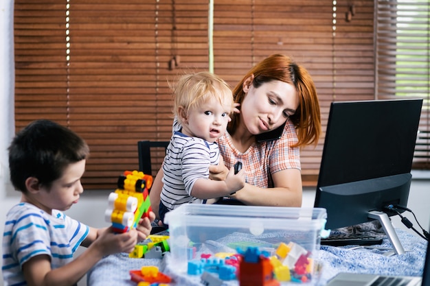 Die junge Mutter versucht leider, während der Zeit der Selbstisolation in Verbindung mit einem Computer an einer entfernten Arbeit zu arbeiten