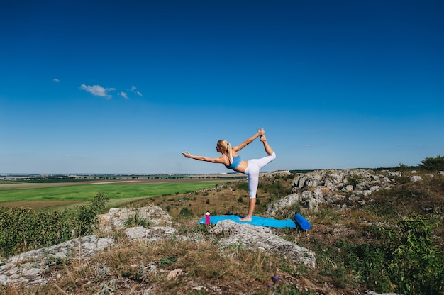 Die junge schöne Blondine, die Yoga tun, trainiert auf einem Felsen. Handstand. Fitness-Studio und Outdoor-Sport