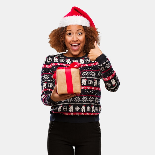Die junge schwarze Frau, die ein Geschenk am Weihnachtstag überrascht hält, fühlt sich erfolgreich und wohlhabend
