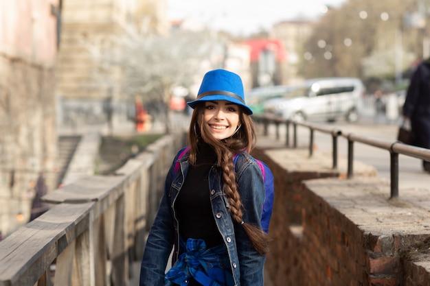 Die junge stilvolle Frau, die auf die alte Stadtstraße geht, reisen mit Rucksack und blauem Hut. Ukraine, Lemberg