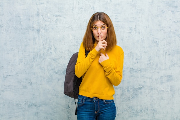 Die junge Studentenfrau, die ernst und mit dem Finger kreuzend schaut, drückte zu den Lippen, die Ruhe oder Ruhe fordern und hielt ein Geheimnis