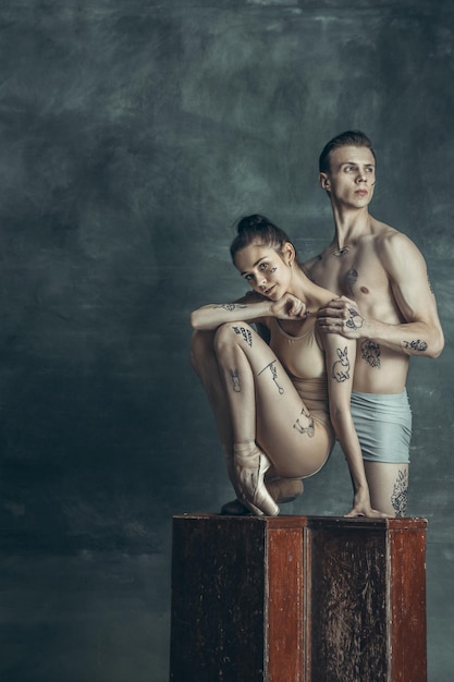 Die jungen modernen Balletttänzer mit Tätowierungen auf Körpern, die auf grauem Studiohintergrund posieren