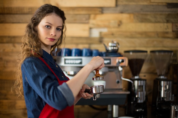 Die Kellnerin drückt mit einem Stampfer gemahlenen Kaffee in einen Siebträger