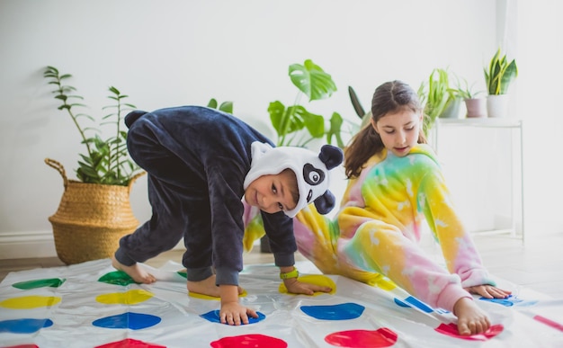 Die Kinder, die in Tier-Kigurumi gekleidet sind, sitzen auf dem Boden im Zimmer. Die Kinder im Schlafanzug spielen Twister