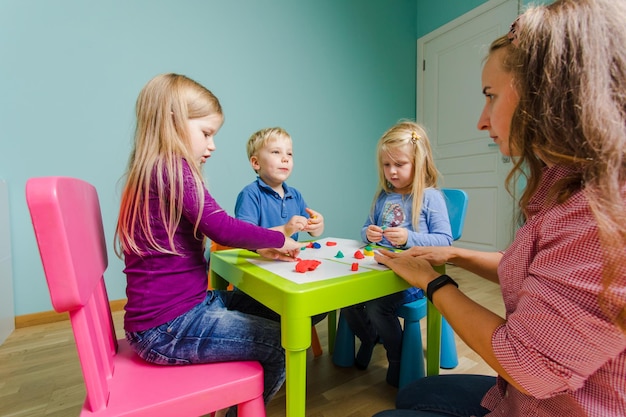 Die Kinder sitzen an den Bänken im Kindergarten und formen mit Plastilin verschiedene Figuren