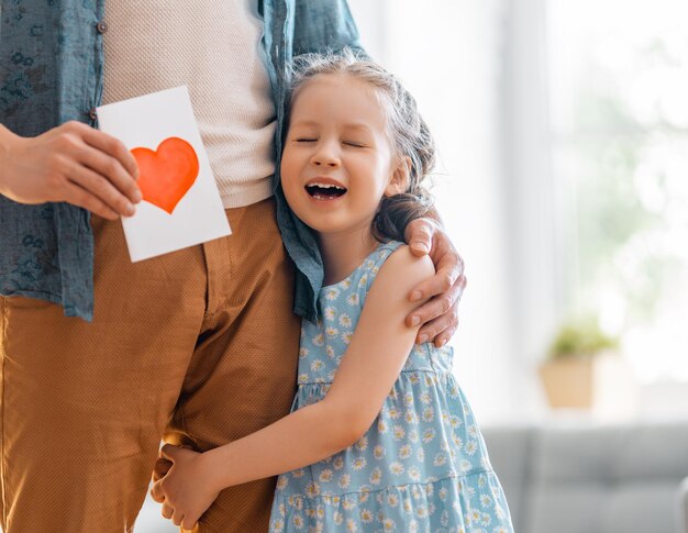 Die kleine Tochter gratuliert ihrem Vater und gibt ihm eine Postkarte Papa und Mädchen lächeln