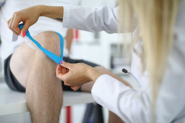 Die Krankenschwester klebt Kinesio-Klebeband auf das Knie des Patienten