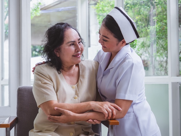 Die Krankenschwester kümmert sich glücklich um ältere Menschen, die Pflegekraft umarmt die alte Frau