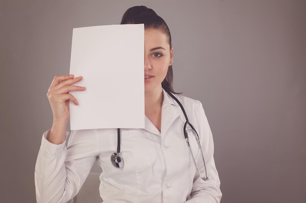 Die Krankenschwester verbirgt ihr Gesicht mit einem Papier vor grauem Hintergrund