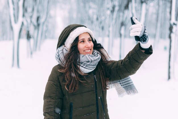 Die lächelnde junge Frau macht ein Selfie in einem schneebedeckten Wald