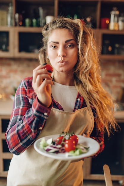 Die lächelnde junge Hausfrau in der Schürze bereitet den Salat zu