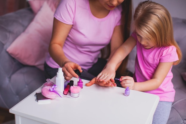 Die lächelnde junge Mutter und ihre Tochter zeigen ihre rosa Maniküre Frau und Mädchen tragen rosa Kleidung und sitzen im Zimmer