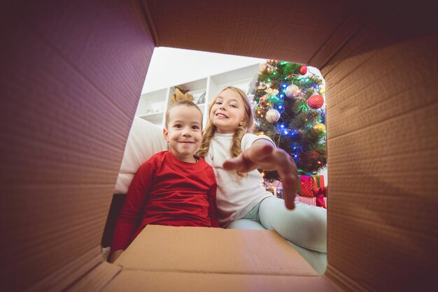 Die Lächelnkinder öffnen die Kiste neben dem Weihnachtsbaum