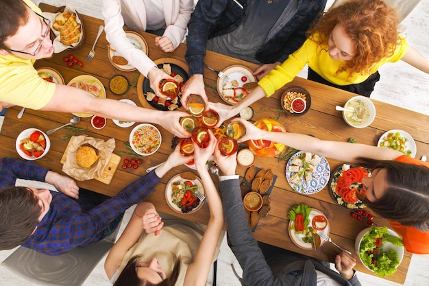 Die Leute stoßen mit den Gläsern an, sagen Prost, essen gesunde Mahlzeiten am Party-Dinner. Freunde feiern mit Bio-Lebensmitteln, Ratatoille und Maisgrill auf Holztisch-Draufsicht.