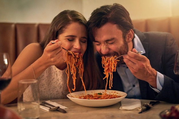 Die Liebe verzehrt alles Aufnahme eines jungen Paares, das sich während eines romantischen Abendessens in einem Restaurant einen Teller Spaghetti teilt