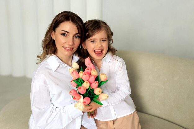 Die liebevolle kleine Tochter gibt ihrer Mutter einen Strauß rosa Tulpen und umarmt sie. Muttertagsfeier oder 8. März