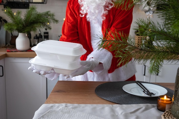 Die Lieferung von Lebensmitteln an Home-Service-Container in den Händen des Weihnachtsmanns legt sie auf den Küchentisch und nimmt sie weg Fertige heiße Bestellung Weihnachten Neujahrsferien Catering