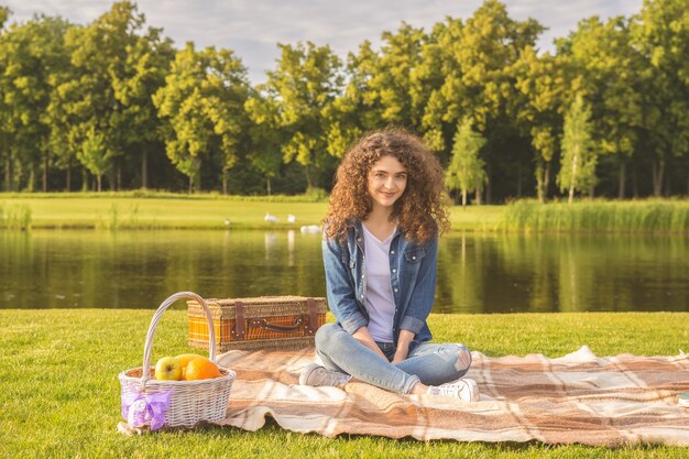 Die lockige Frau ruht sich bei einem Picknick in der Nähe des Flusses aus