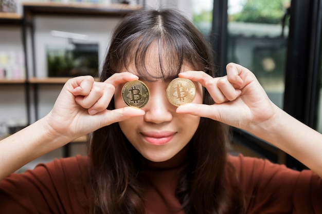 Die lustige Geschäftsfrau, die ein goldenes Bitcoin und Litecoin hält, schloss ihr Auge