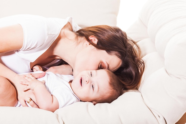 Die Mama küsst hübsches Baby ins Ohr, das auf der Couch liegt