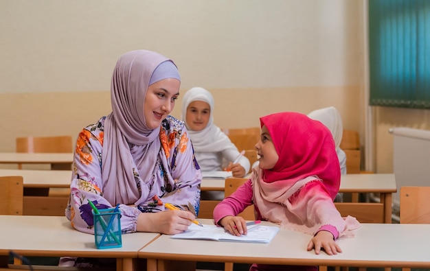 Die muslimische Hijab-Lehrerin hilft Schulkindern, den Unterricht im Klassenzimmer zu beenden.