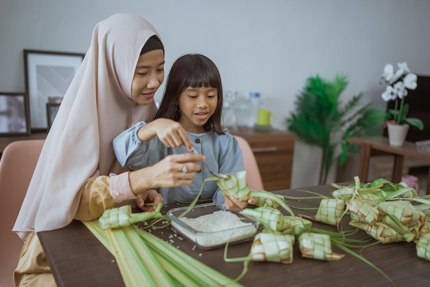 Die muslimische Mutter bringt ihrer Tochter bei, wie man ein Ketupat für Eid Mubarak macht