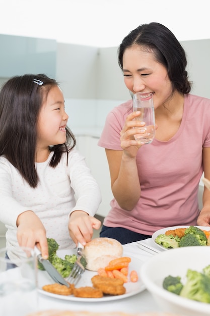 Die Mutter, die kleines Mädchen aufpasst, essen Lebensmittel in der Küche