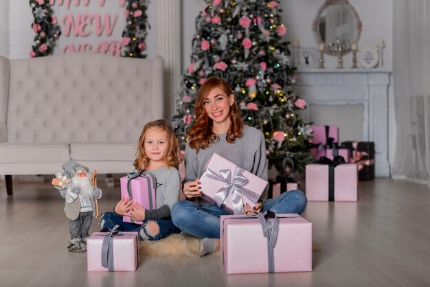 Die Mutter und die Tochter sitzen auf dem Boden in der Nähe des Weihnachtsbaums