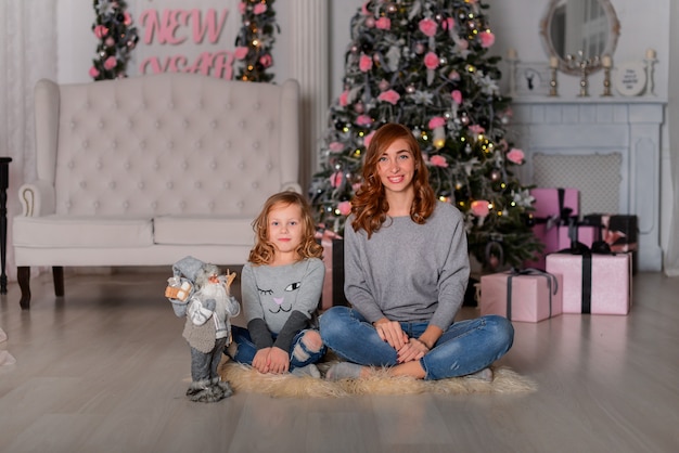 Die Mutter und Tochter in der Nähe von Weihnachtsbaum sitzen auf dem Boden