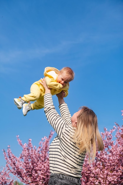 Die Mutter wirft das Baby in ihren Armen in den Himmel