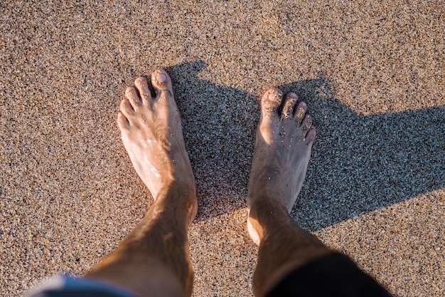 Die nackten Füße der Männer stehen am Sandstrand. Ansicht von oben, flach.