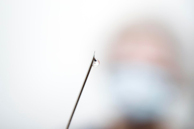 Die Nadel aus der Spritze mit einem Tropfen am Ende im Hintergrund verwischte den Patienten