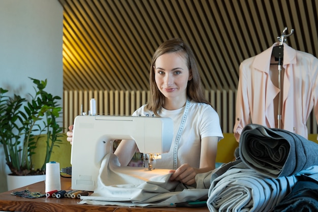 Die Näherin der jungen Frau näht auf einer Nähmaschine, die an einem Tisch sitzt