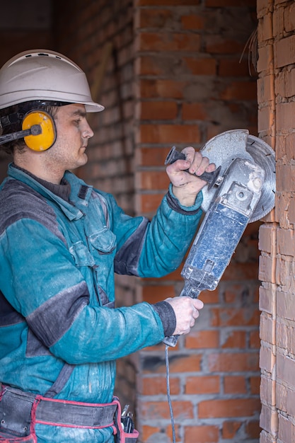 Die Nahaufnahme eines Bauherrn in einem Schutzhelm an einer Arbeitseinrichtung arbeitet mit einem Schneidwerkzeug.