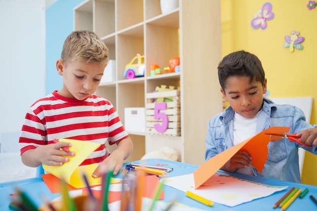 Die netten kleinen Jungen, die Papier schneiden, formt in Klassenzimmer