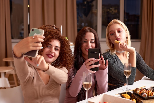 Die neuesten Klatsch und Tratsch diskutieren Drei schöne junge Frauen reden und lächeln, während sie Wein trinken und zusammen auf der Couch sitzen