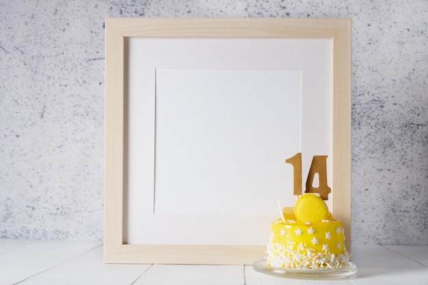 Die Nummer Vierzehn auf dem gelben Kuchen neben dem weißen Rahmenmodell mit Kopierraum